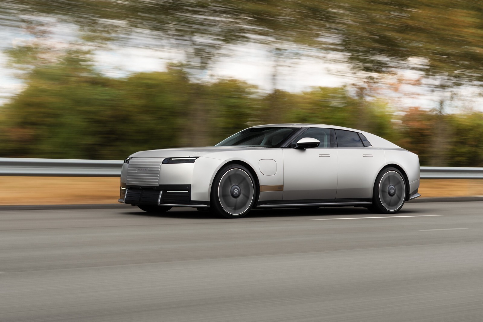 Jaguar Type 01 eléctrico blanco en movimiento, visto de perfil en una carretera.