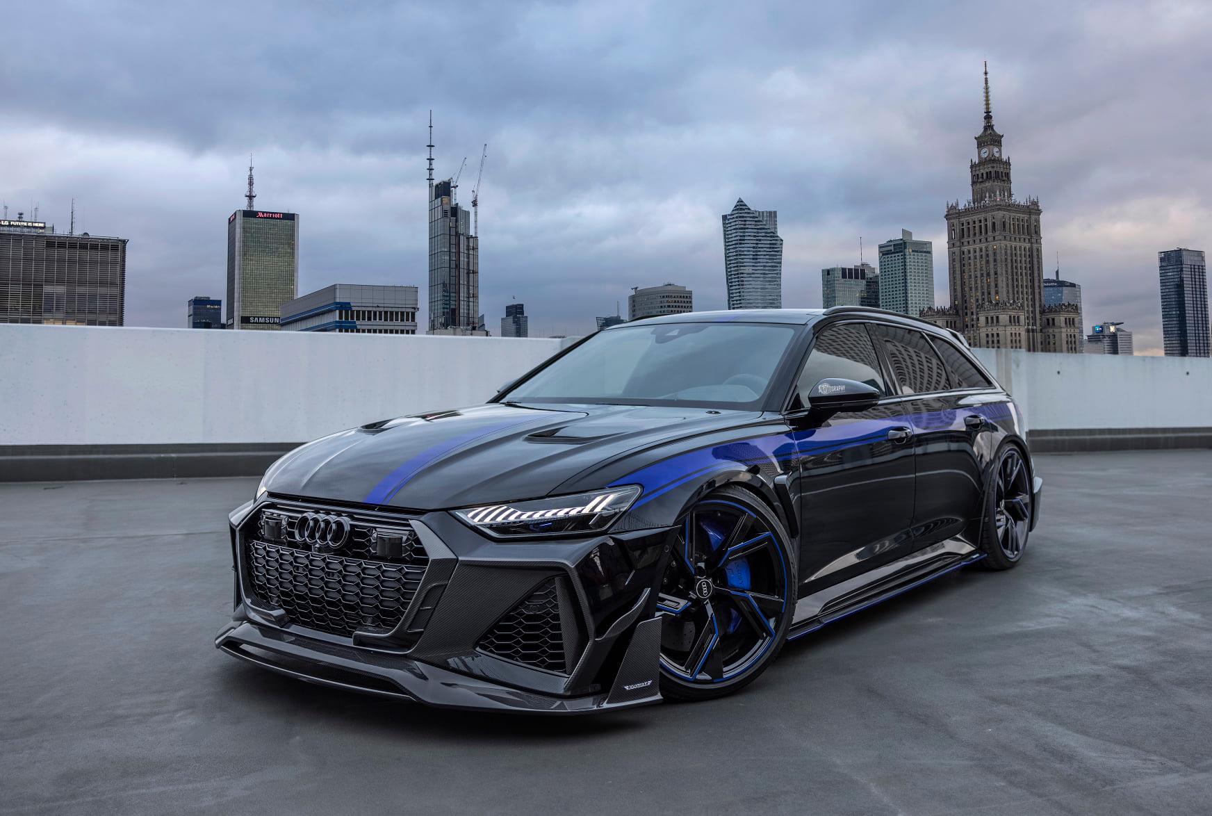 Audi RS6 Avant negro de MTM y Mansory en vista frontal de tres cuartos, con edificios al fondo.