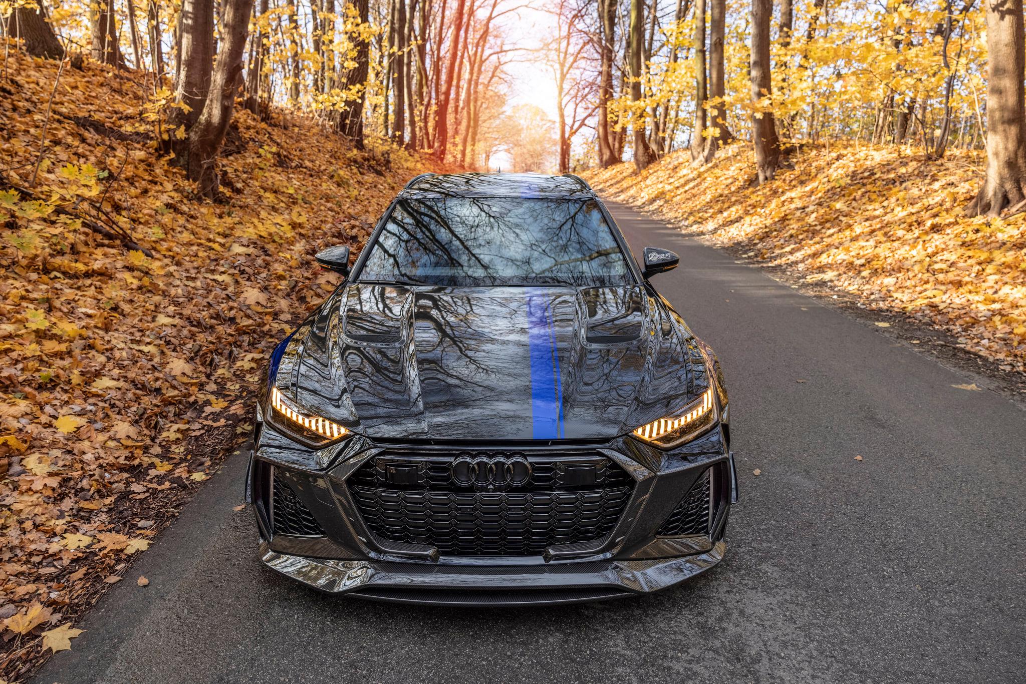 Audi RS6 Avant de MTM y Mansory de frente en una carretera rodeada de árboles otoñales.
