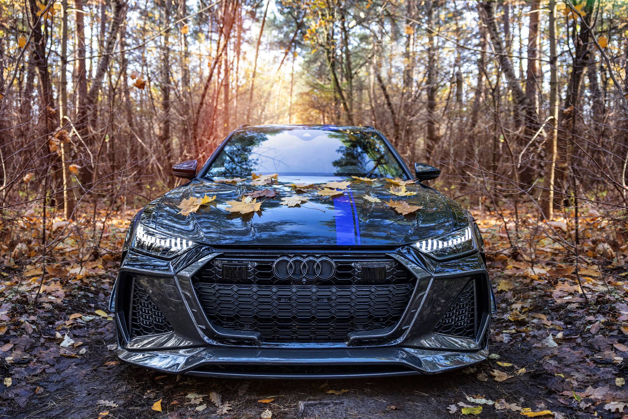 Frontal del Audi RS6 Avant de MTM y Mansory entre hojas caídas en un camino de bosque.