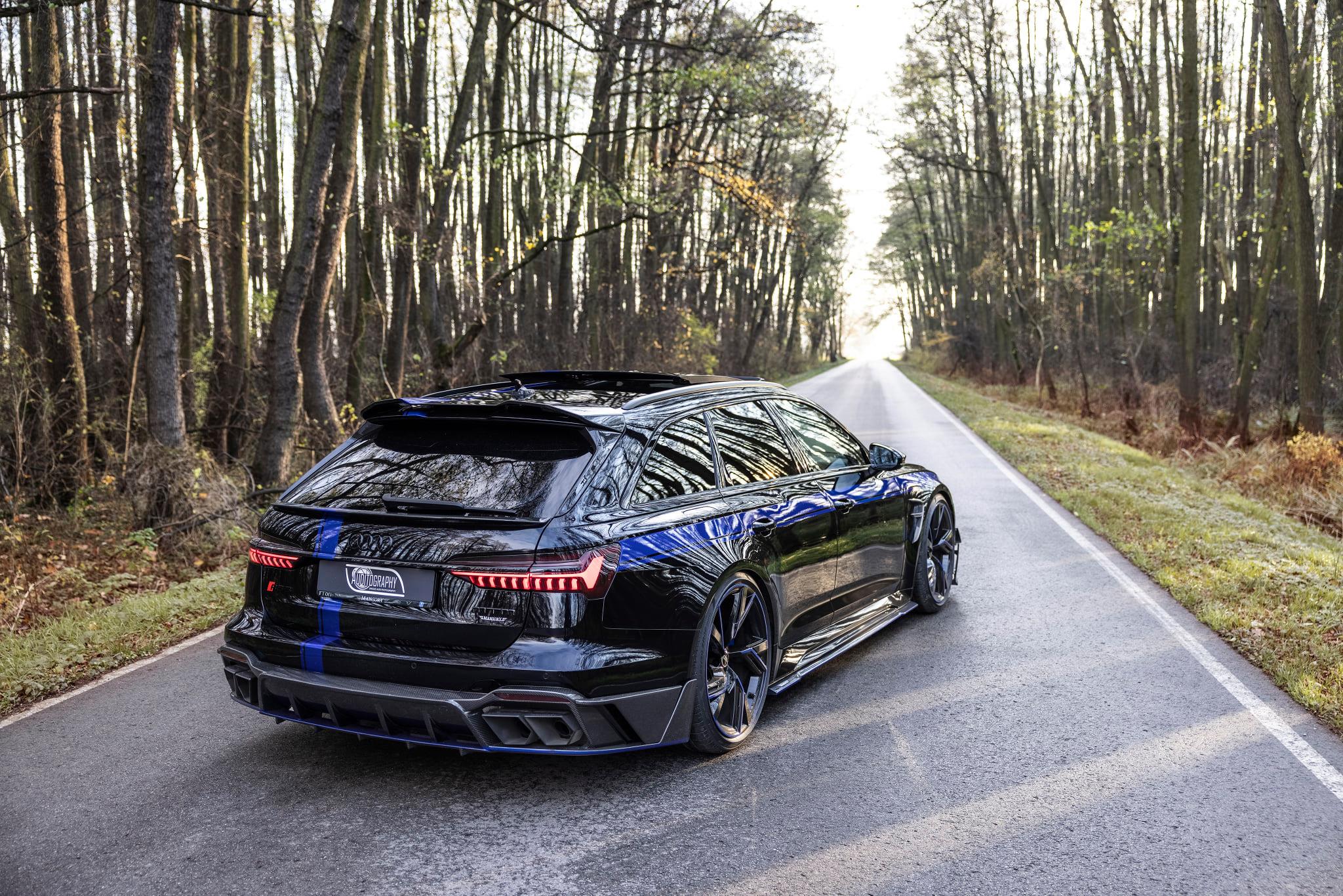 Audi RS6 Avant negro de MTM y Mansory visto desde atrás en una carretera boscosa.