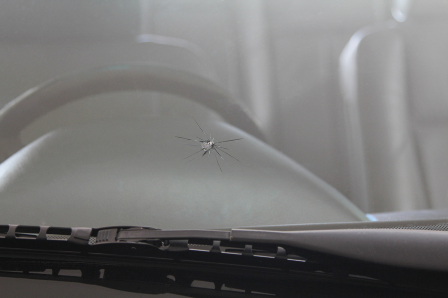 Damaged car front windshield with cracks caused by splashing debris.
