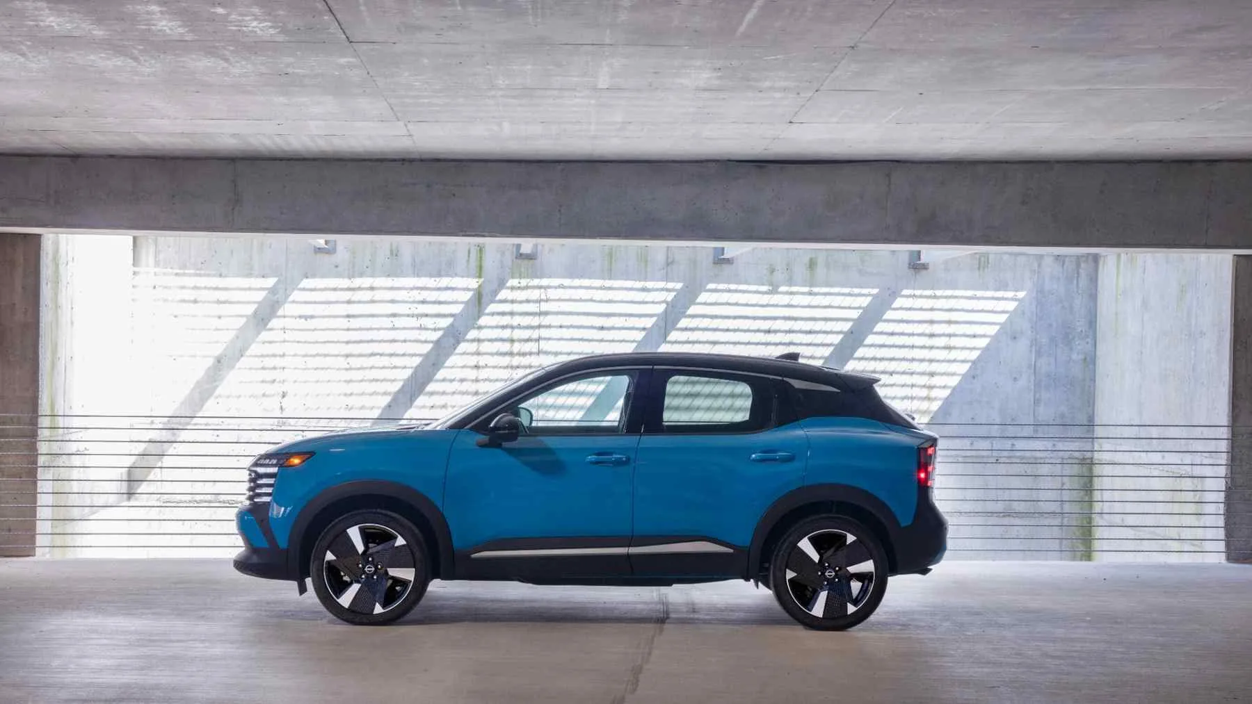 Nissan Kicks azul de perfil en un espacio arquitectónico de hormigón.