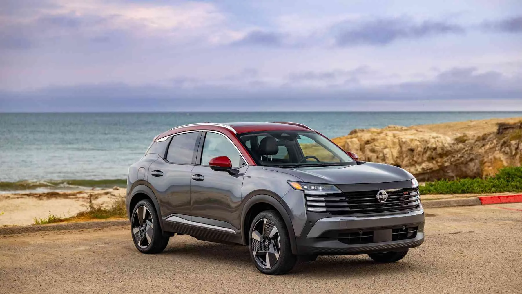 Nissan Kicks gris con techo rojo en vista frontal de tres cuartos junto al mar.